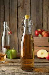 Photo of Delicious cider in glass bottle and apples on wooden table, closeup