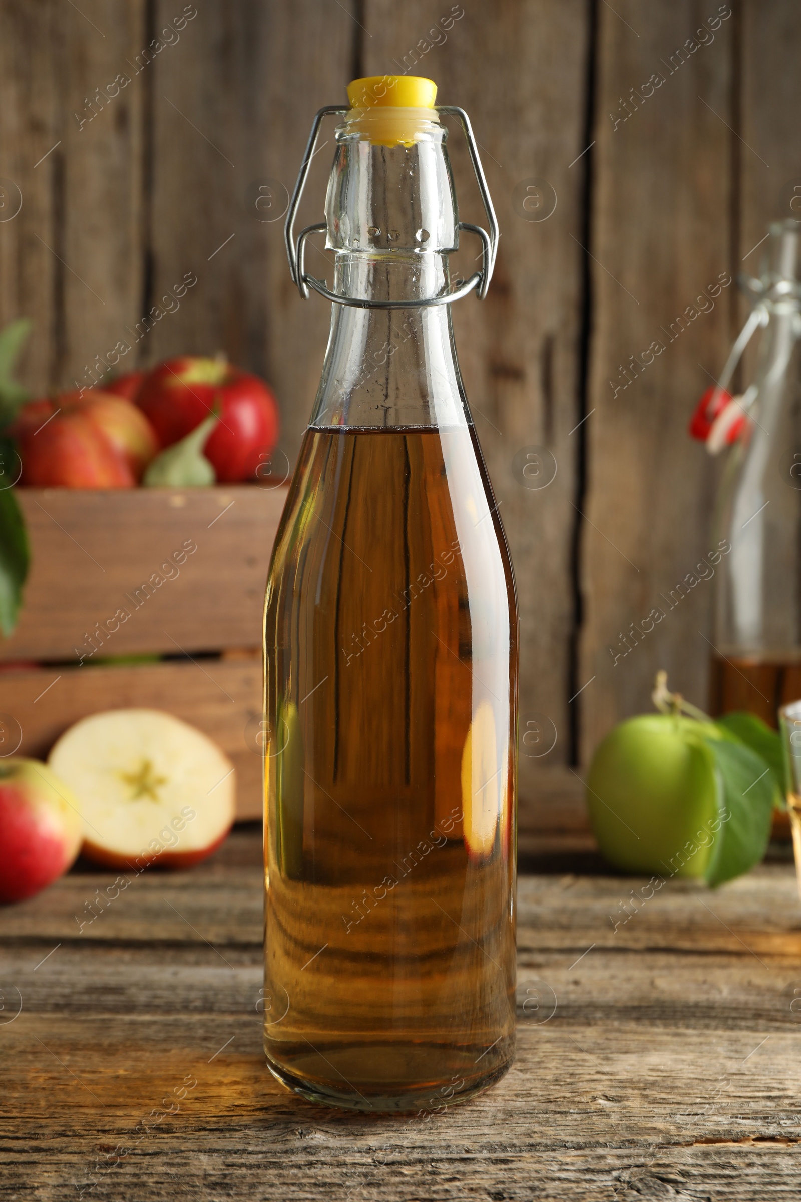 Photo of Delicious cider in glass bottle and apples on wooden table, closeup