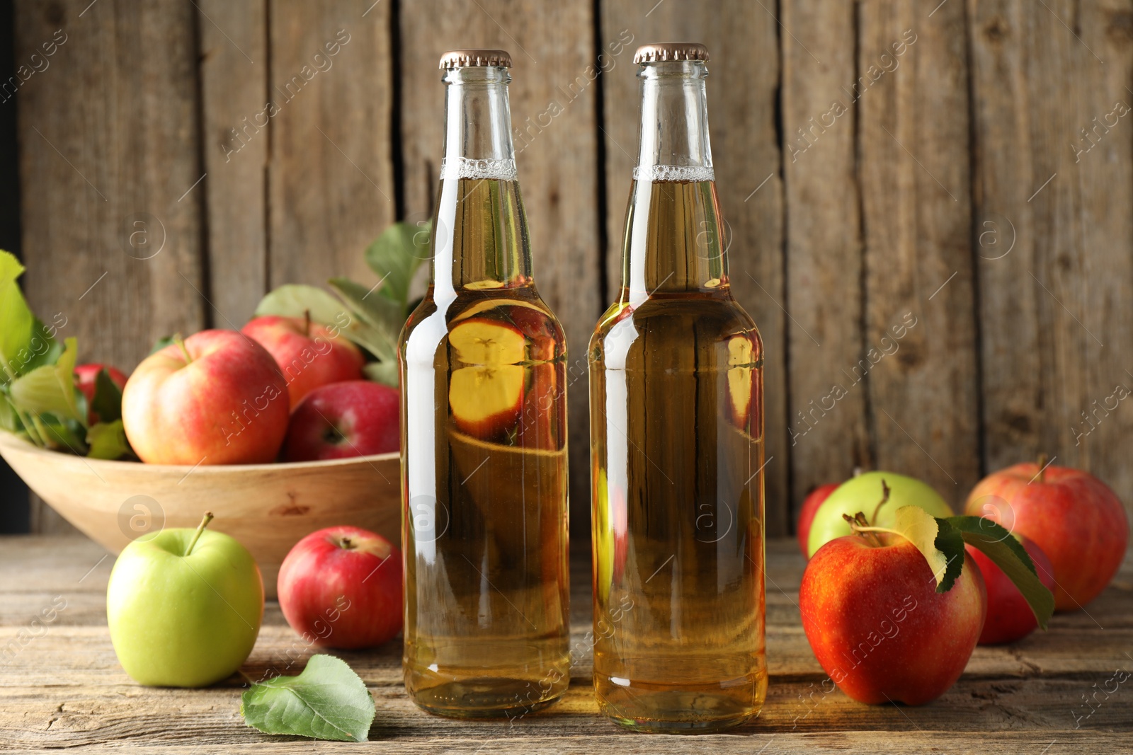 Photo of Delicious cider in glass bottles and apples on wooden table