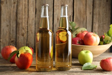 Photo of Delicious cider in glass bottles and apples on wooden table