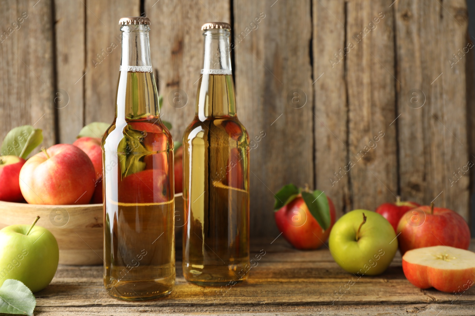 Delicious cider in glass bottles and apples on wooden table. Space for text Photo of Delicious cider in glass bottles and apples on wooden table. Space for text