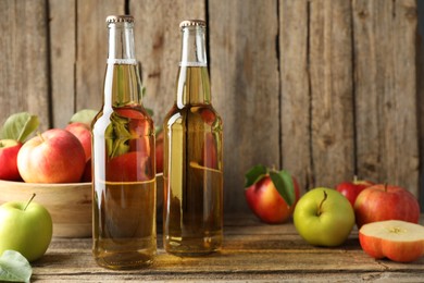 Photo of Delicious cider in glass bottles and apples on wooden table. Space for text