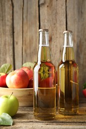 Photo of Delicious cider in glass bottles and apples on wooden table