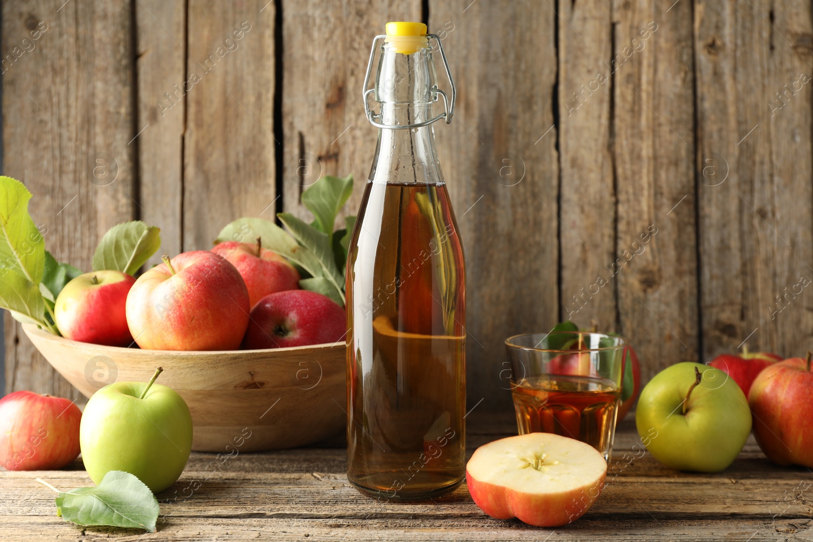 Photo of Delicious cider in bottle, glass and apples on wooden table