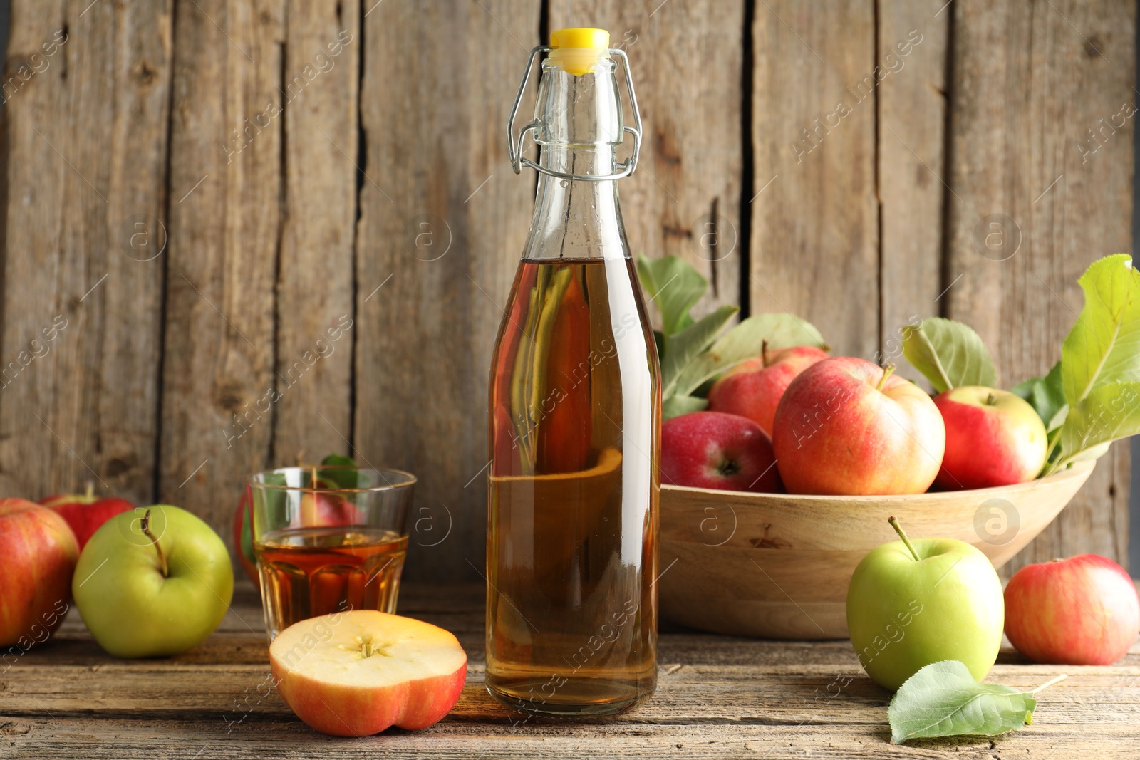 Photo of Delicious cider in bottle, glass and apples on wooden table