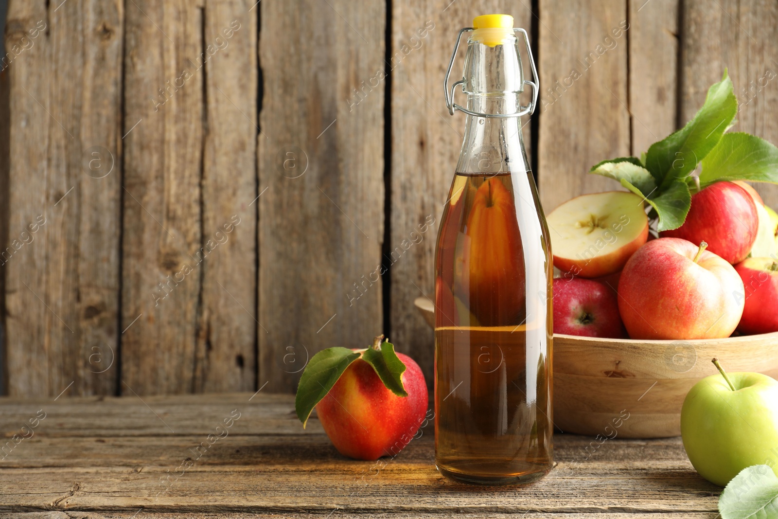Photo of Delicious cider in glass bottle and apples on wooden table. Space for text