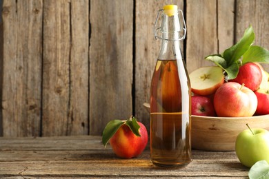 Photo of Delicious cider in glass bottle and apples on wooden table. Space for text