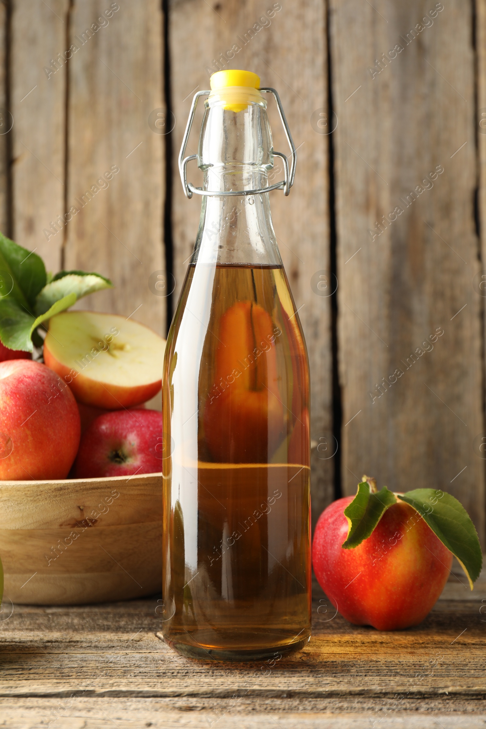 Photo of Delicious cider in glass bottle and apples on wooden table