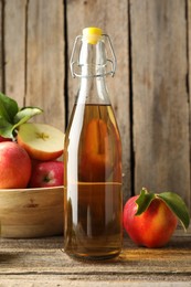 Photo of Delicious cider in glass bottle and apples on wooden table