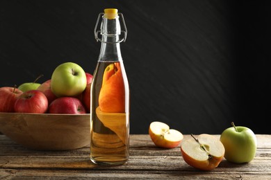 Photo of Delicious cider in glass bottle and apples on wooden table against dark gray background. Space for text
