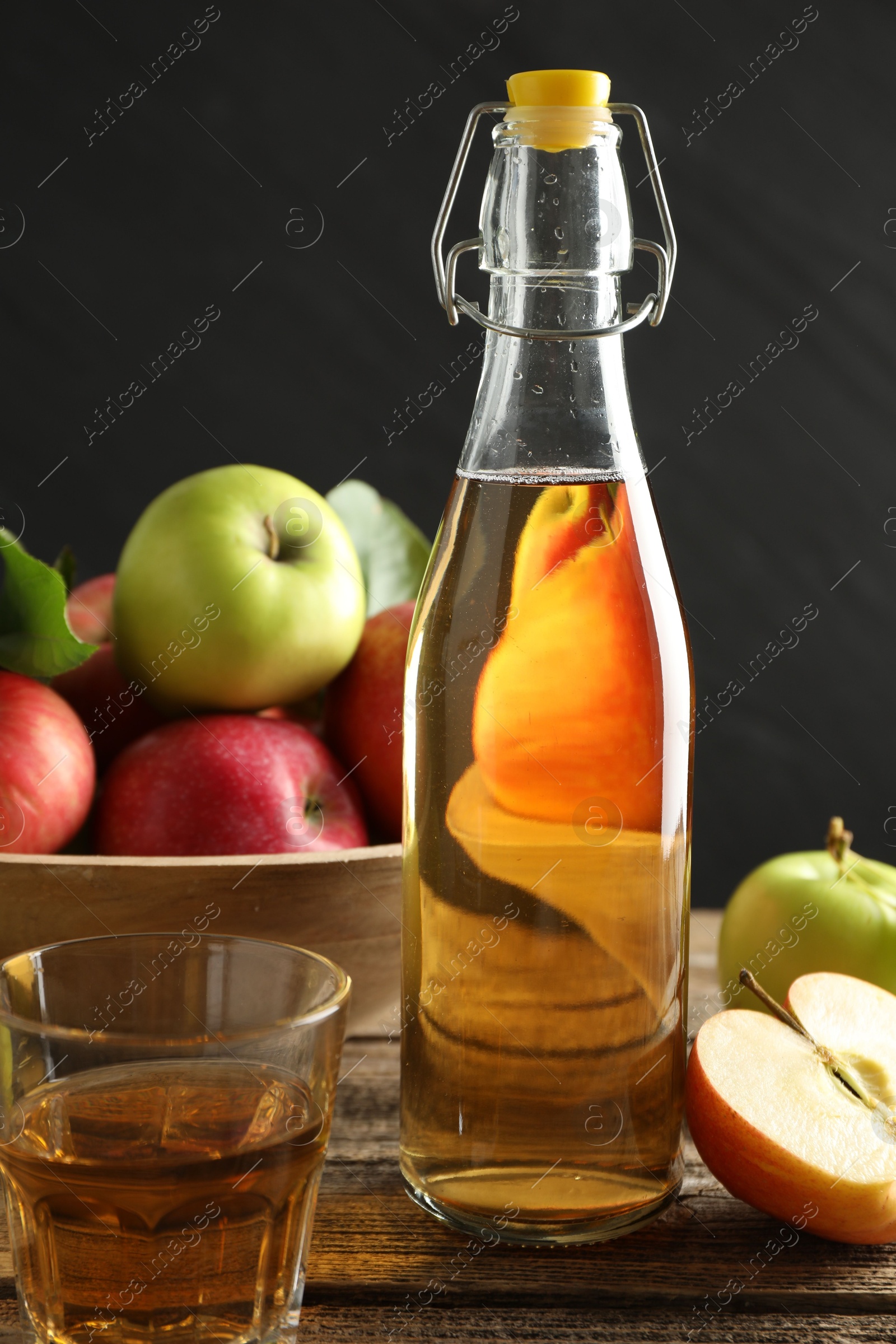 Delicious cider in bottle, glass and apples on wooden table against dark gray background, closeup Photo of Delicious cider in bottle, glass and apples on wooden table against dark gray background, closeup