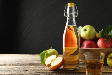 Photo of Delicious cider in bottle, glass and apples on wooden table against dark gray background. Space for text