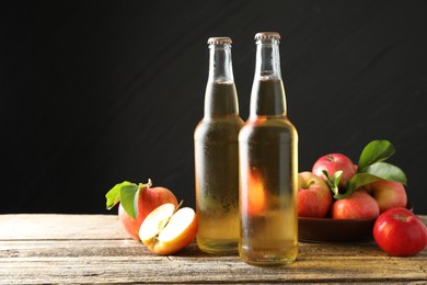 Photo of Delicious cider in glass bottles and apples on wooden table against dark gray background. Space for text