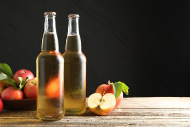 Photo of Delicious cider in glass bottles and apples on wooden table against dark gray background. Space for text