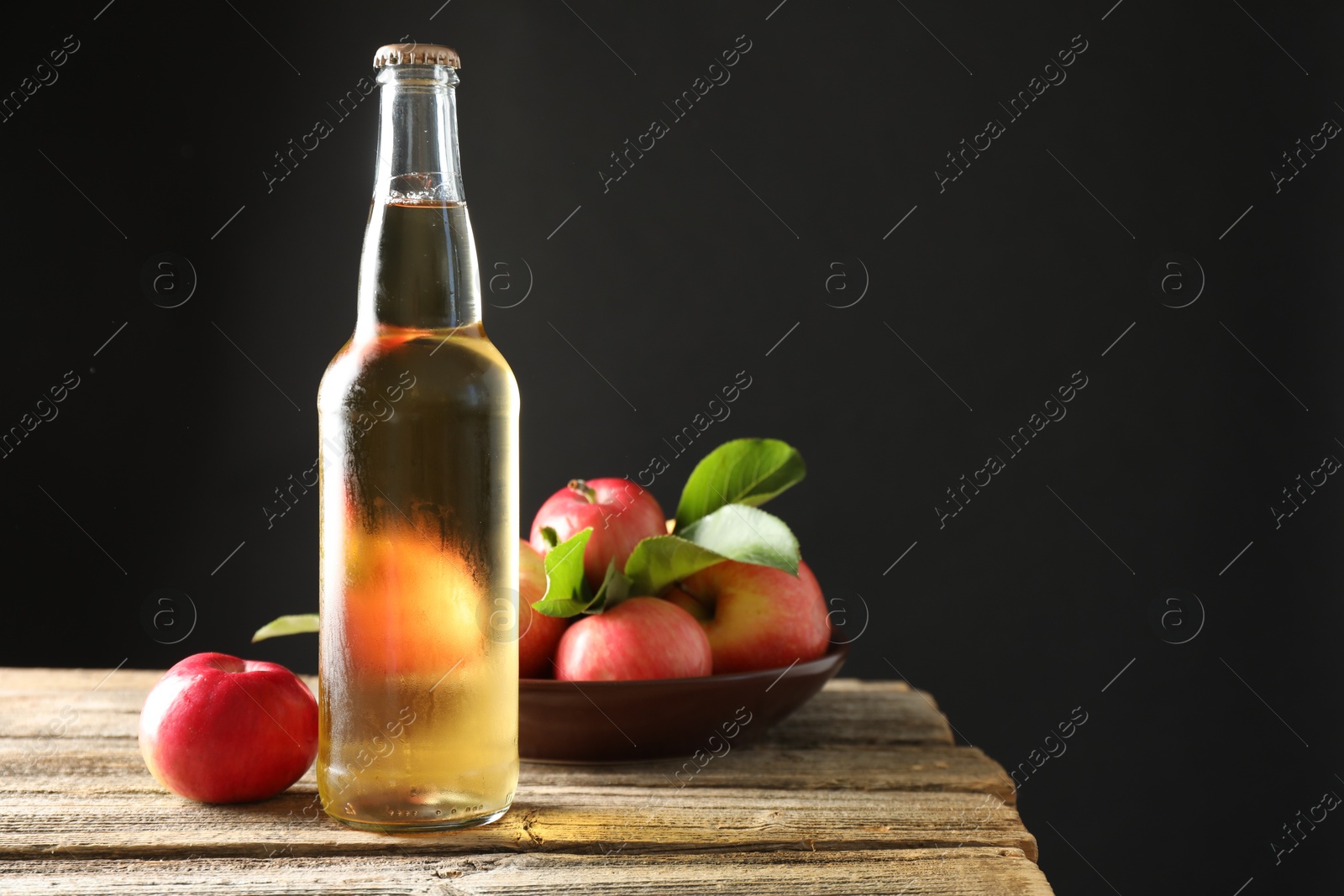 Delicious cider in glass bottle and apples on wooden table against dark gray background. Space for text Photo of Delicious cider in glass bottle and apples on wooden table against dark gray background. Space for text