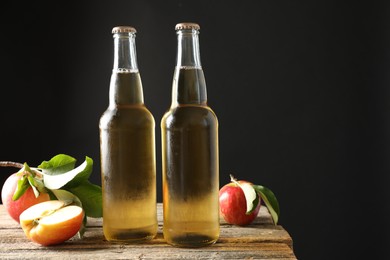 Photo of Delicious cider in glass bottles and apples on wooden table against dark gray background. Space for text