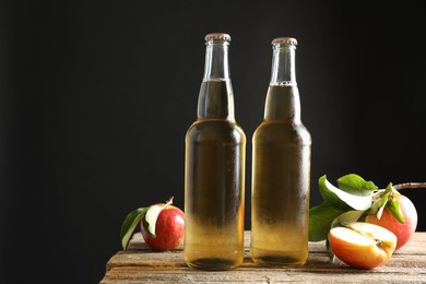 Photo of Delicious cider in glass bottles and apples on wooden table against dark gray background. Space for text