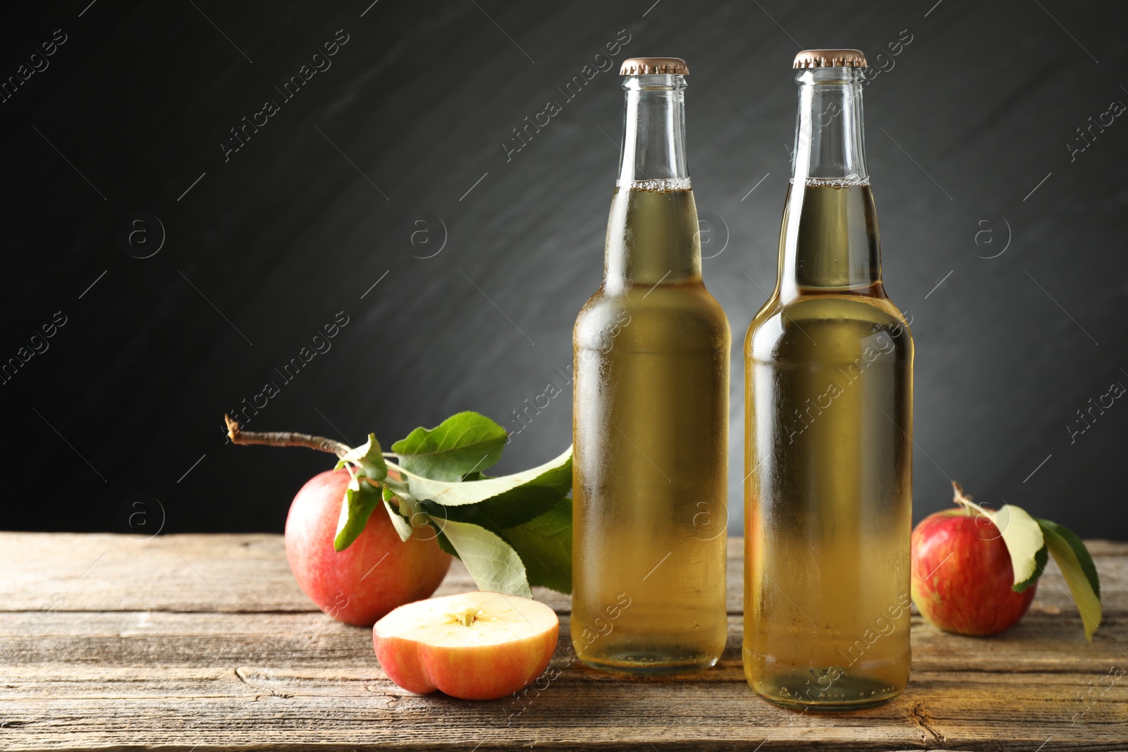 Delicious cider in glass bottles and apples on wooden table against dark gray background. Space for text Photo of Delicious cider in glass bottles and apples on wooden table against dark gray background. Space for text