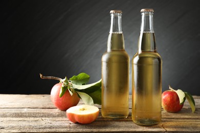 Photo of Delicious cider in glass bottles and apples on wooden table against dark gray background. Space for text
