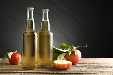 Photo of Delicious cider in glass bottles and apples on wooden table against dark gray background. Space for text