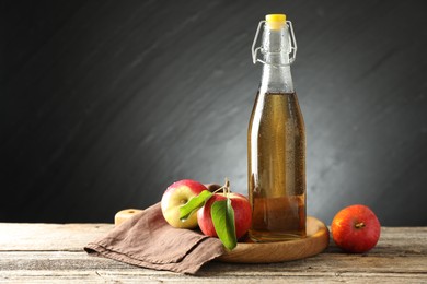 Photo of Delicious cider in glass bottle and apples on wooden table against dark gray background. Space for text