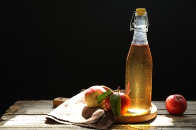 Photo of Delicious cider in glass bottle and apples on wooden table against dark background. Space for text
