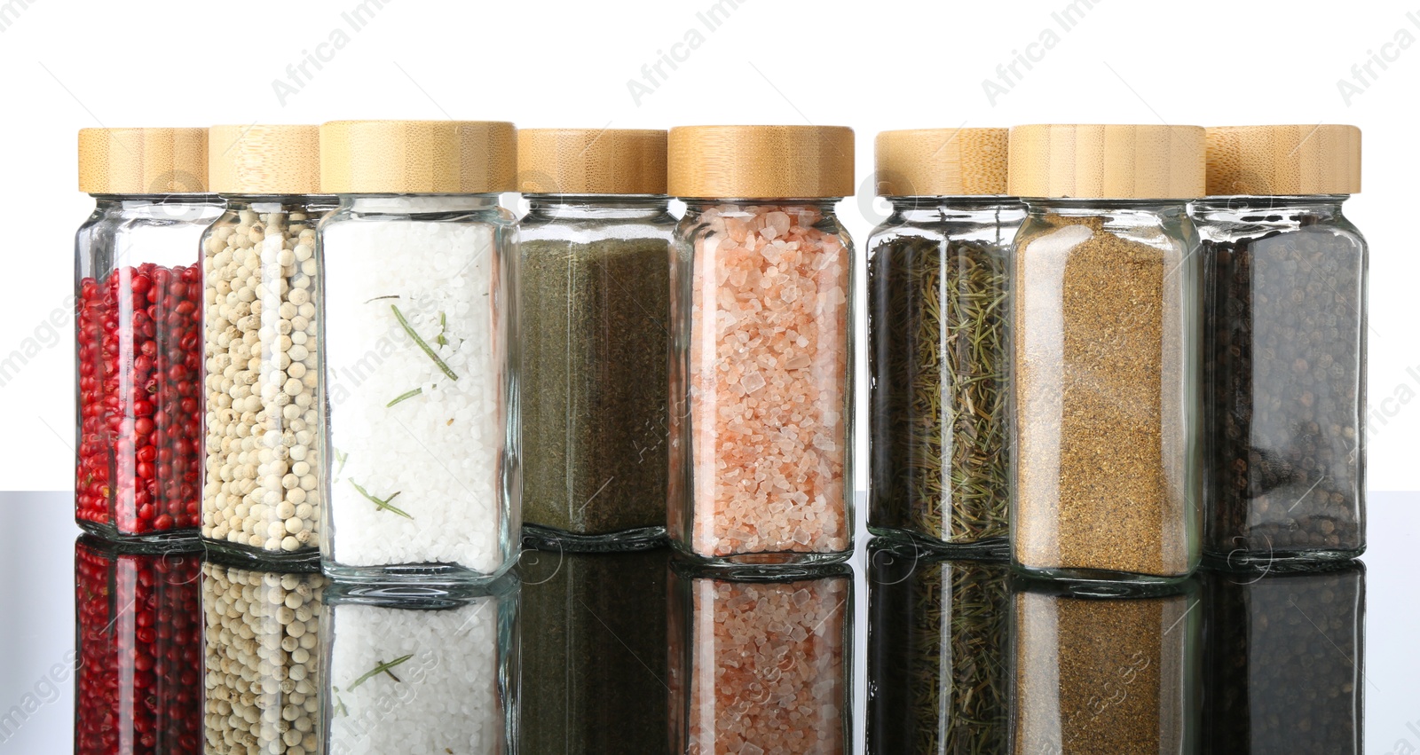 Photo of Different spices in jars on mirror surface against white background