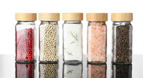 Photo of Different spices in jars on mirror surface against white background