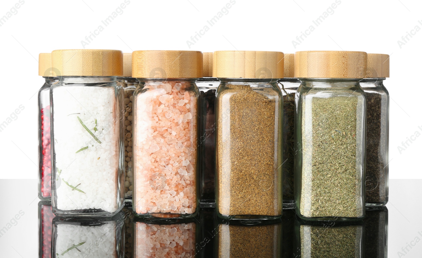 Photo of Different spices in jars on mirror surface against white background