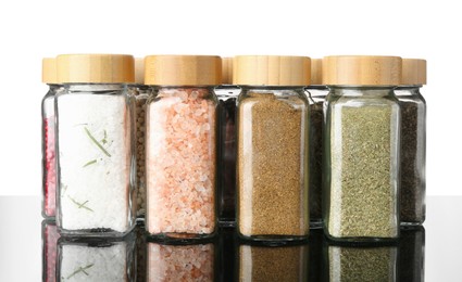 Photo of Different spices in jars on mirror surface against white background