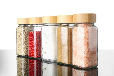 Photo of Different spices in jars on mirror surface against white background