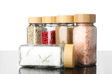 Photo of Different spices in jars on mirror surface against white background