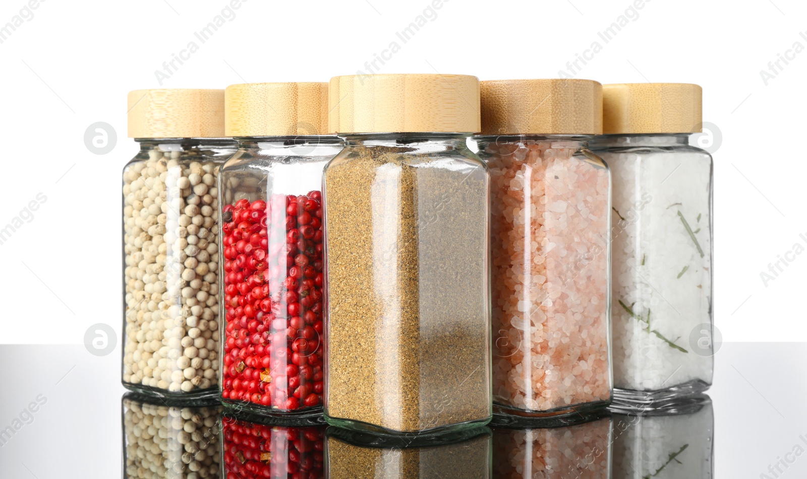 Photo of Different spices in jars on mirror surface against white background