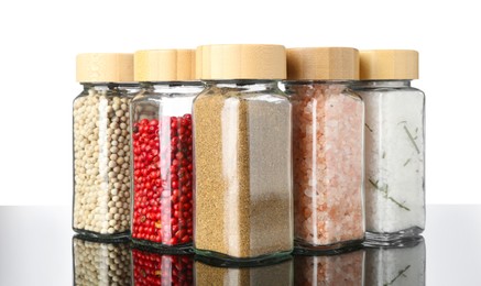 Photo of Different spices in jars on mirror surface against white background