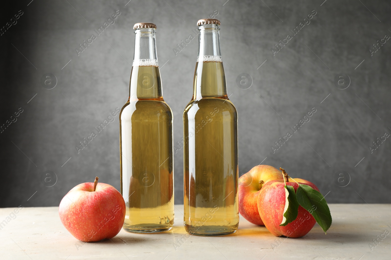 Photo of Delicious cider in glass bottles and apples on table against gray background