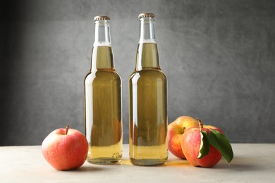 Photo of Delicious cider in glass bottles and apples on table against gray background
