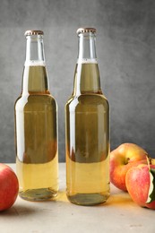 Photo of Delicious cider in glass bottles and apples on table against gray background
