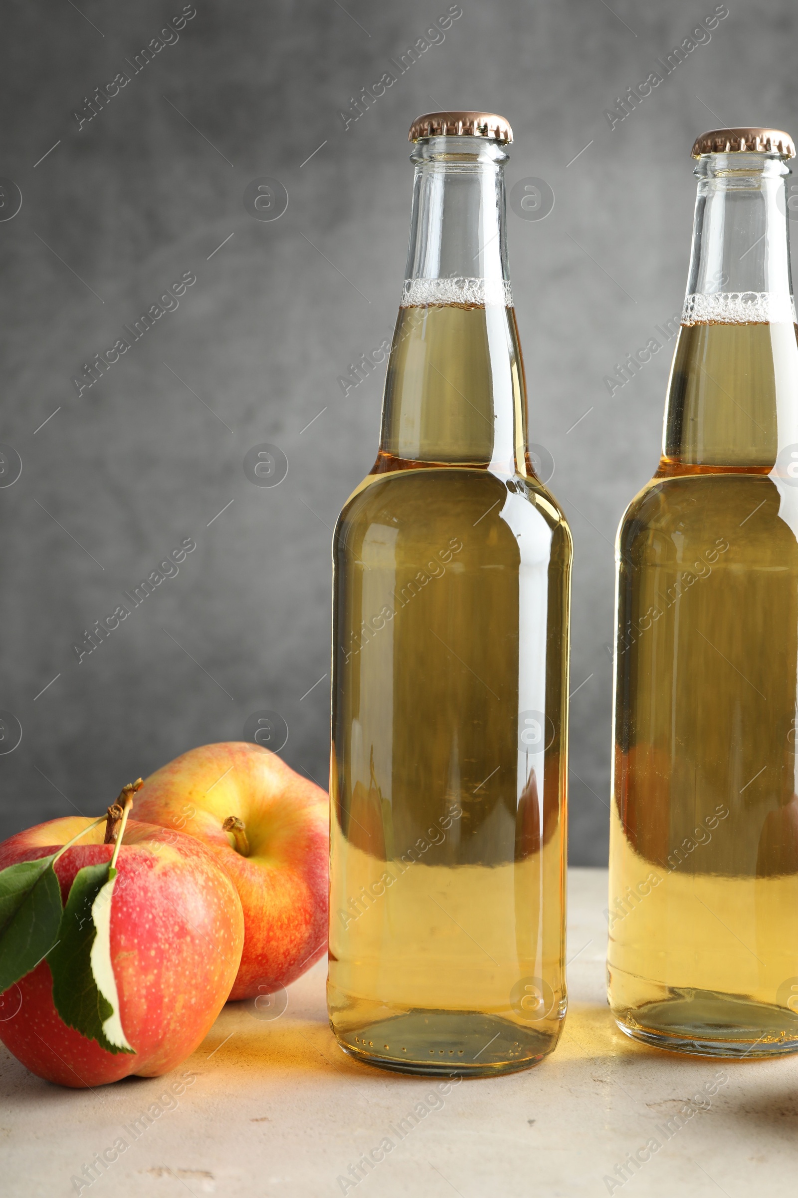 Photo of Delicious cider in glass bottles and apples on table against gray background, closeup