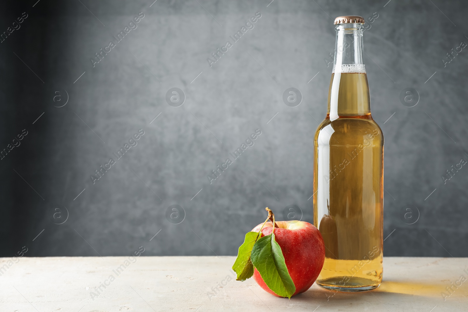 Photo of Delicious cider in glass bottle and apple on table against gray background. Space for text