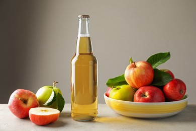 Photo of Delicious cider in glass bottle and apples on gray table against light background