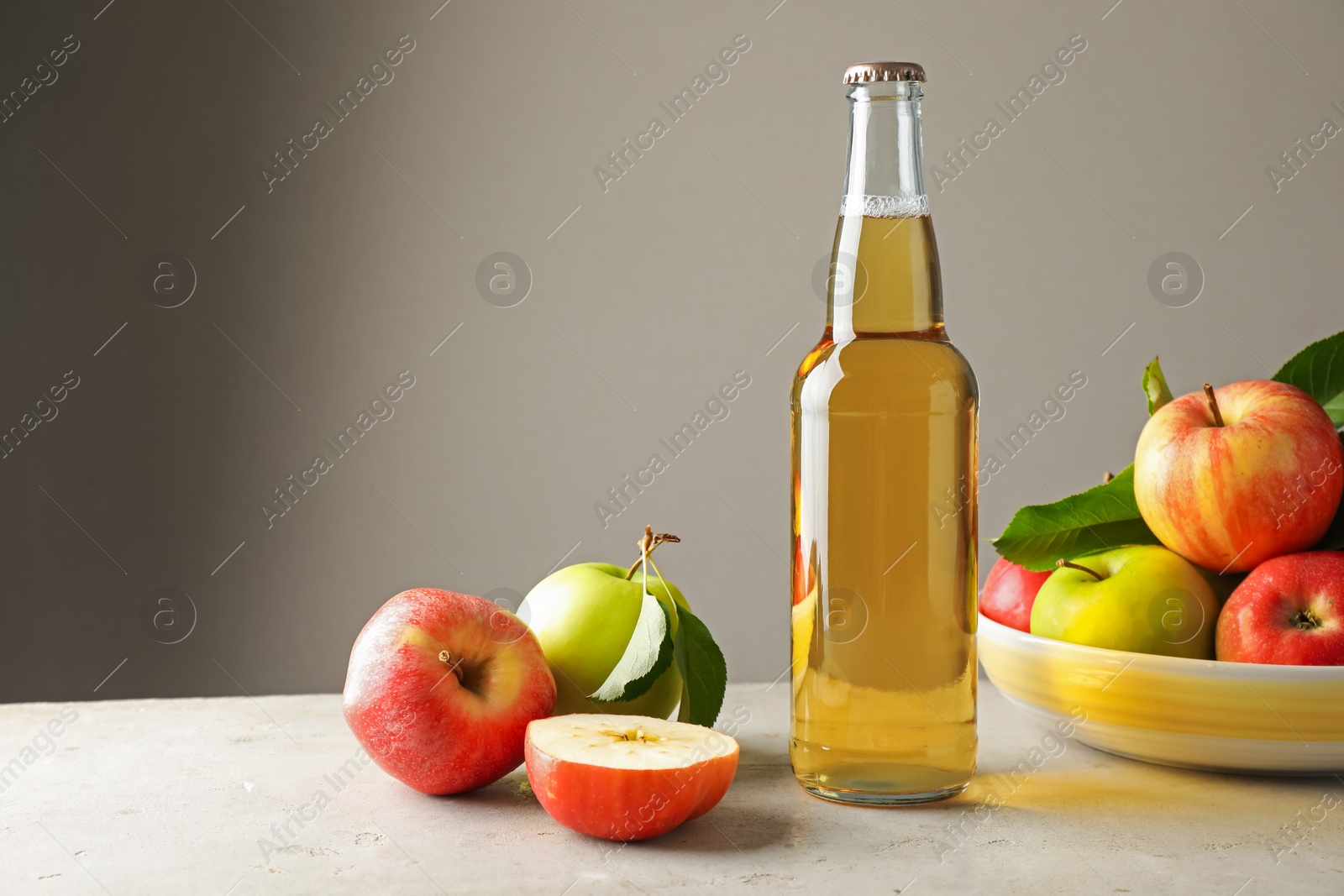 Photo of Delicious cider in glass bottle and apples on gray table against light background. Space for text
