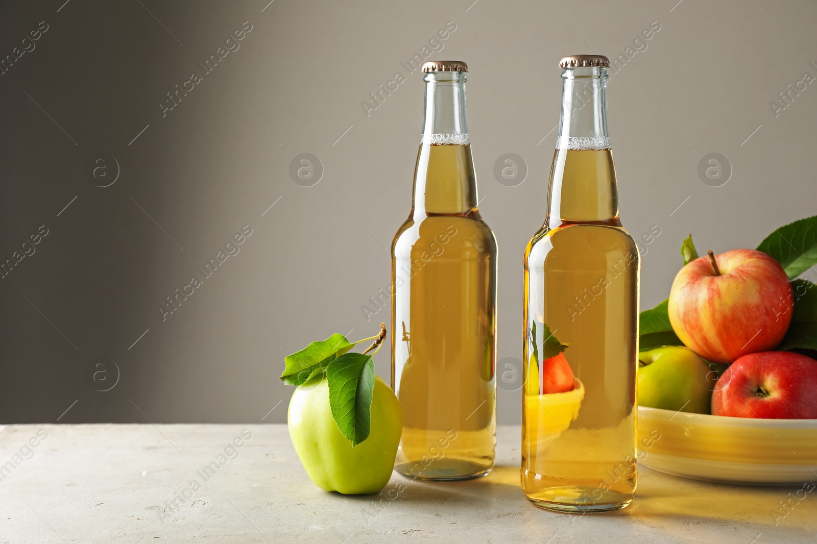 Delicious cider in glass bottles and apples on gray table against light background. Space for text Photo of Delicious cider in glass bottles and apples on gray table against light background. Space for text