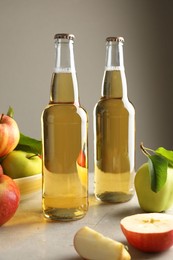 Photo of Delicious cider in glass bottles and apples on gray table against light background