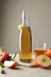 Photo of Delicious cider in bottle, glass and apples on gray table against light background
