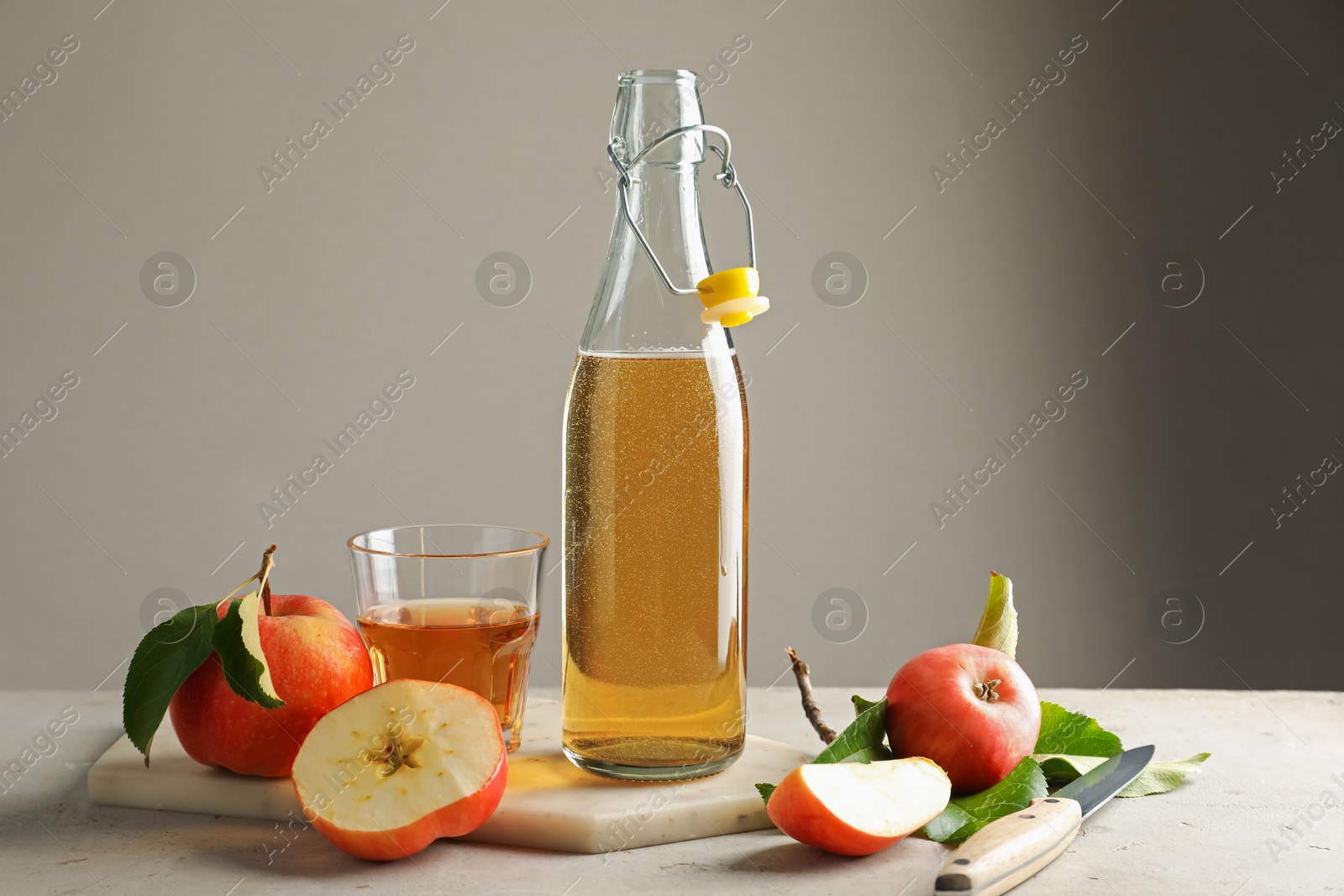 Photo of Delicious cider in bottle, glass and apples on gray table against light background
