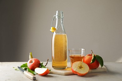 Photo of Delicious cider in bottle, glass and apples on gray table against light background