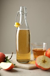Photo of Delicious cider in bottle, glass and apples on gray table against light background