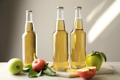 Photo of Delicious cider in glass bottles and apples on gray table against light background