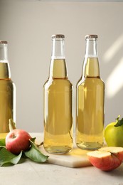Photo of Delicious cider in glass bottles and apples on gray table against light background