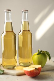 Photo of Delicious cider in glass bottles and apples on gray table against light background